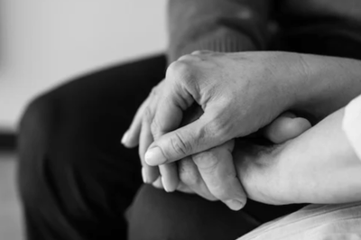 Close-up black and white photo of two people holding hands, symbolizing comfort, care, and support during a difficult time.