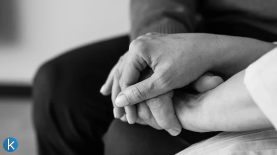 Close-up black and white photo of two people holding hands, symbolizing comfort, care, and support during a difficult time.
