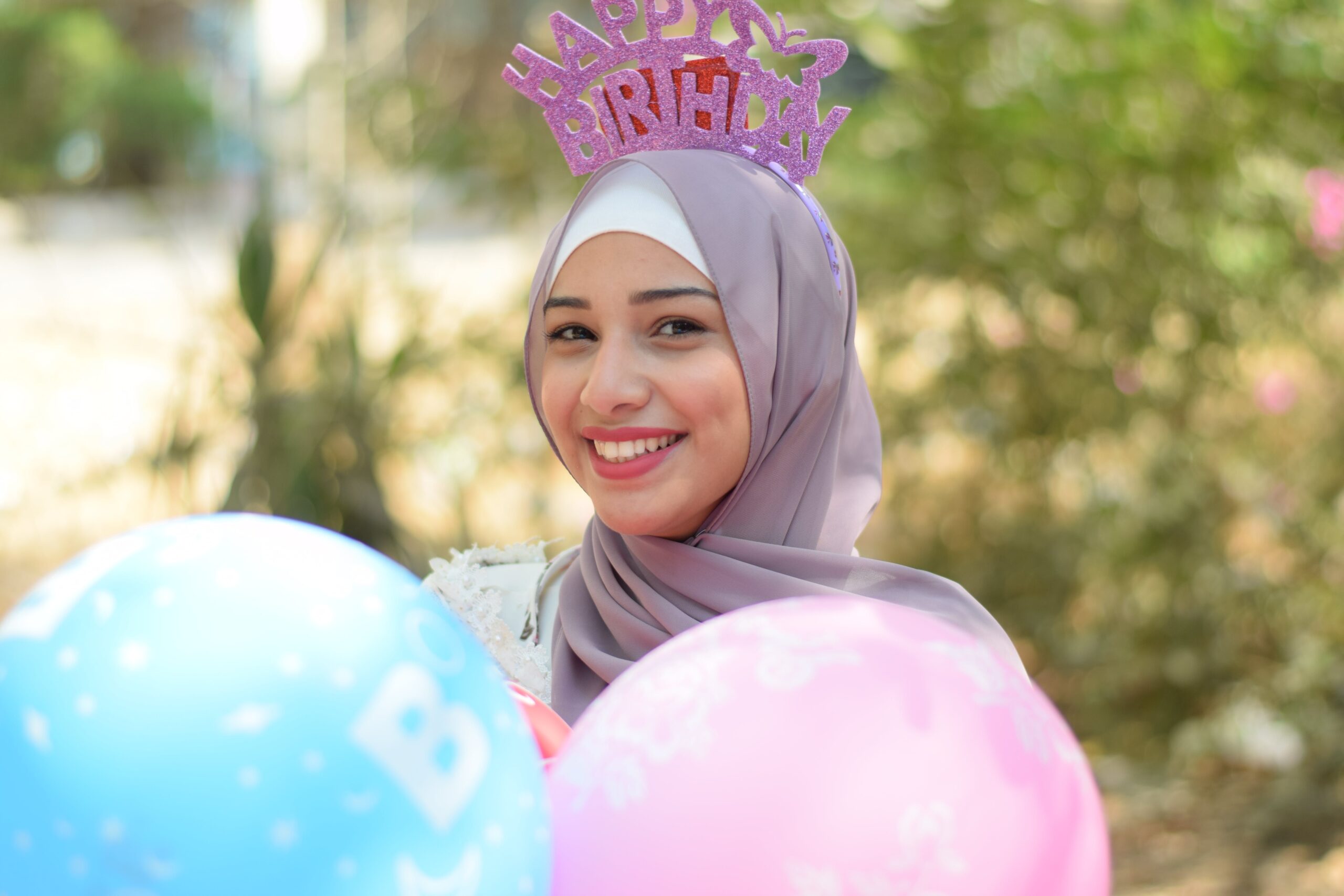 Woman wearing headscarf holding balloons and wearing birthday crown