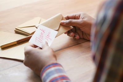 Hands holding an envelope and a card that says "thank you"
