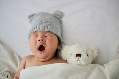 Yawning baby in a hat with a teddy bear