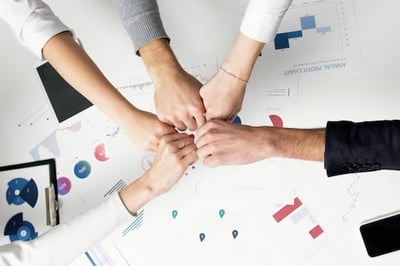 Five fists bumping in the middle of a table with graphs and charts on it