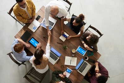 Overhead conference table shot featuring office workers and their laptops on a peer recognition program