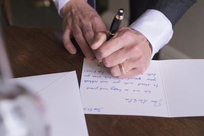 Left handed man wearing tuxedo and ring is writing a group greeting card.