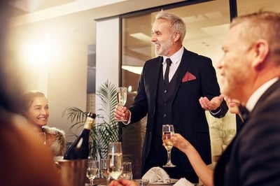 A man standing with a glass of champagne in front of colleagues giving an employee retirement speech