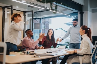 A group of five happy employees gathered around a conference room table smiling
