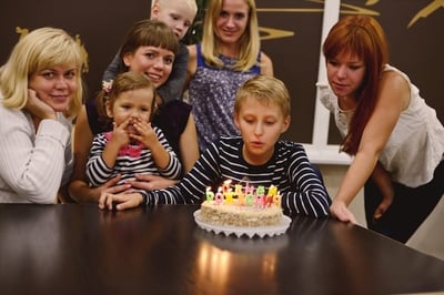 A young boy blowing out candles with his aunt and family while receiving nephew birthday wishes