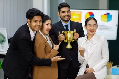 Employee spotlight celebrating diverse coworkers holding a gold trophy together in an office, recognizing team success and achievement