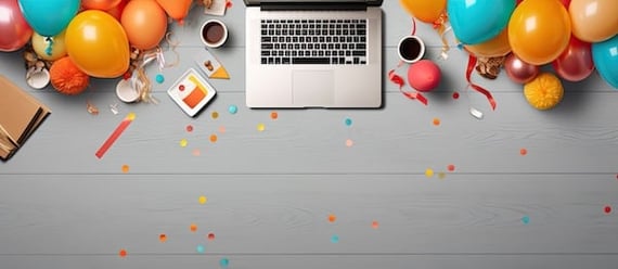 Overhead shot of a laptop with balloons and confetti with a happy work anniversary card