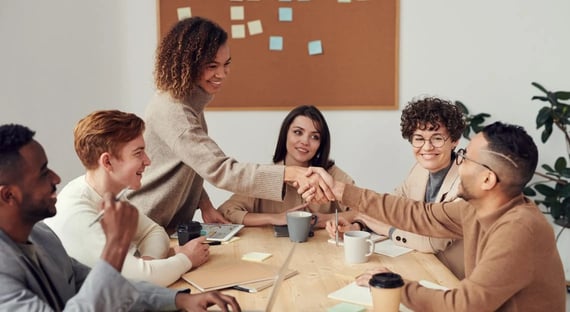 Coworkers shaking hands across table of peers