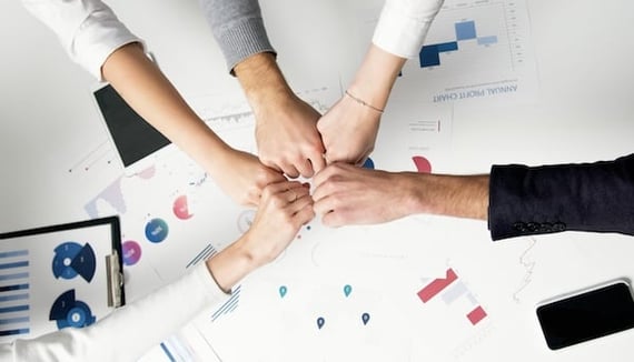 Five fists bumping in the middle of a table with graphs and charts on it