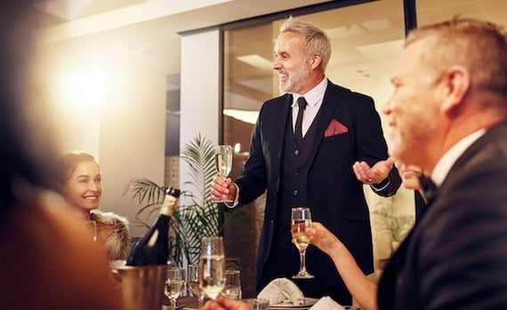 A man standing with a glass of champagne in front of colleagues giving an employee retirement speech