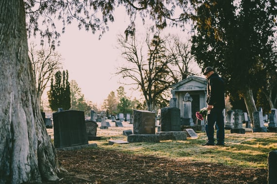 Man placing flowers on gravestone at cemetery