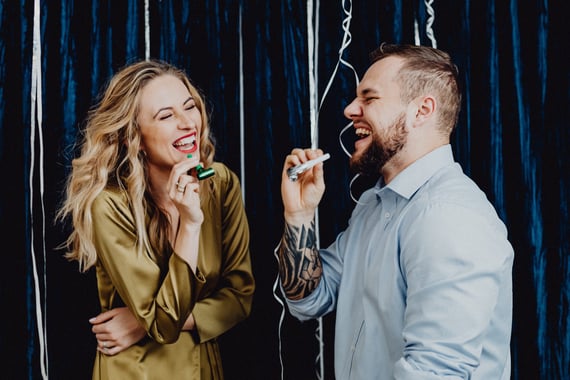 Two people laughing and blowing party horns