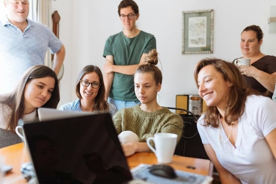 A group of smiling people gathered around a laptop working together on employee recognition