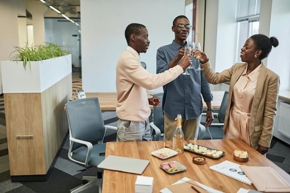 Three employees in a conference room toasting with champagne to a work anniversary