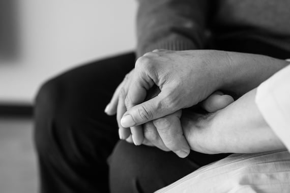 Close-up black and white photo of two people holding hands, symbolizing comfort, care, and support during a difficult time.