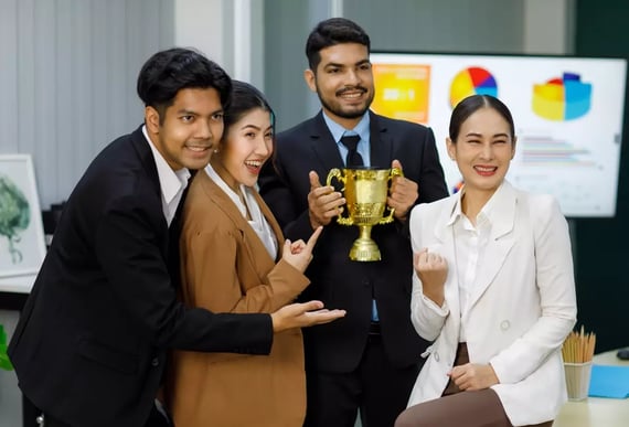 Employee spotlight celebrating diverse coworkers holding a gold trophy together in an office, recognizing team success and achievement
