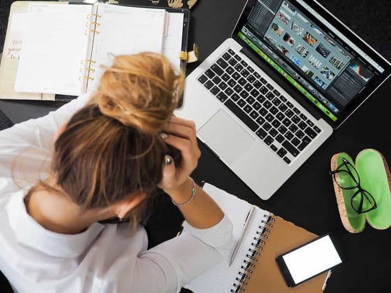 Person sitting with head in hands and working on laptop