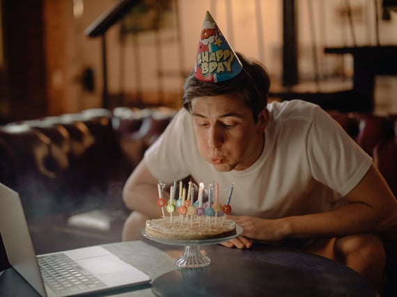 Person blowing out candles on cake in front of laptop