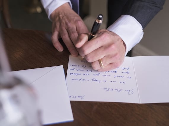 Left handed man wearing tuxedo and ring is writing a group greeting card.
