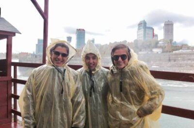 Three people in rain coats standing on boat