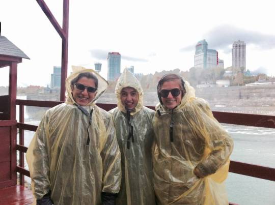 Three people in rain coats standing on boat
