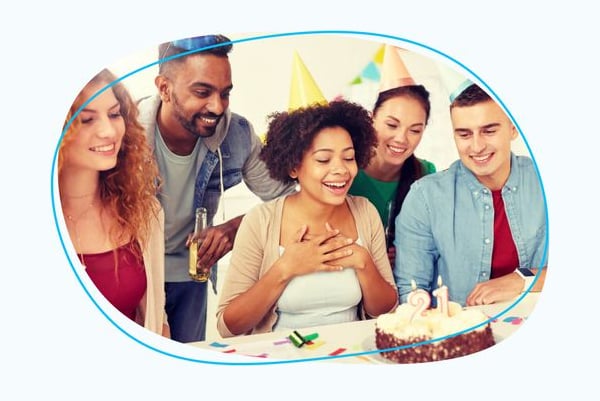 Person about to blow out candles on cake with group of people in party hats