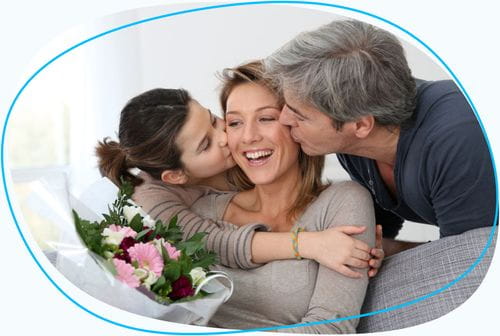 Mother holding flowers being kissed by family