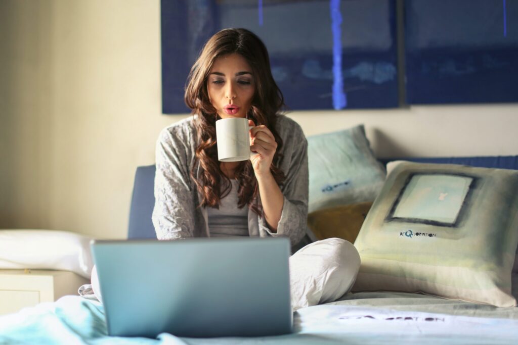 Person working on laptop in bed with mug