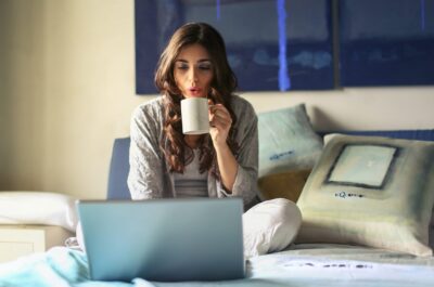 Person working on laptop in bed with mug