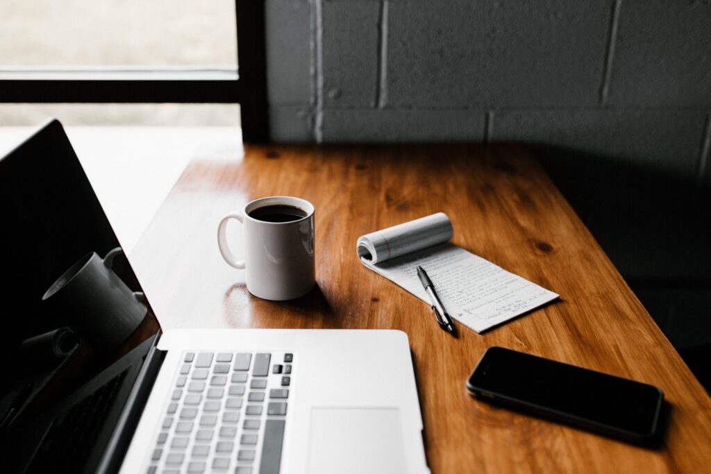 Laptop on desk with coffee cup and notepad