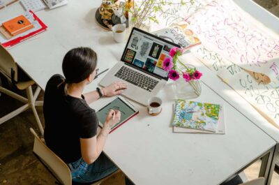 Person at table making art on laptop and tablet