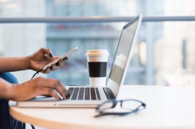 Person working on both phone and laptop at desk