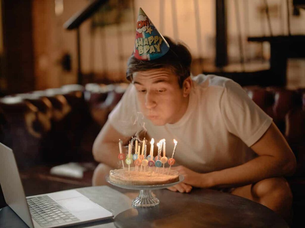 Person wearing birthday hat blowing out candles