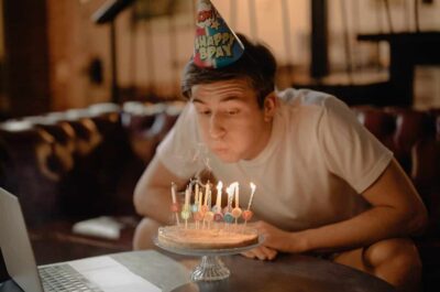 Person wearing birthday hat blowing out candles