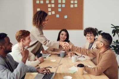 People shaking hands across table of smiling employees