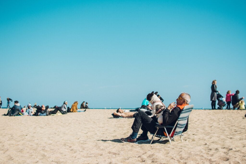 Man sitting in chair with dog at crowded beach