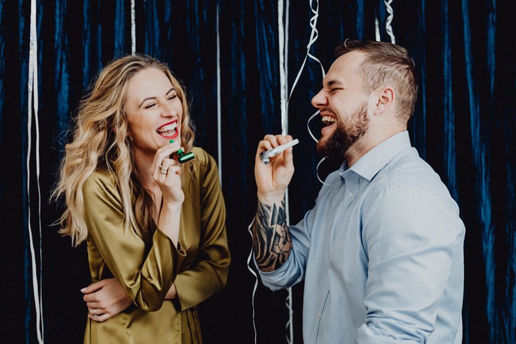 Two people laughing and blowing party horns