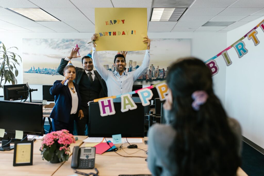 Office workers holding happy birthday sign for surprised coworker