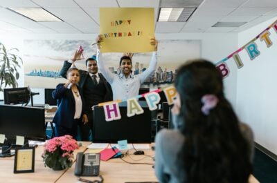 Office workers holding happy birthday sign for surprised coworker