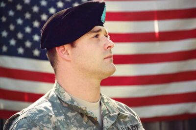 Service member looking away and American flag in background