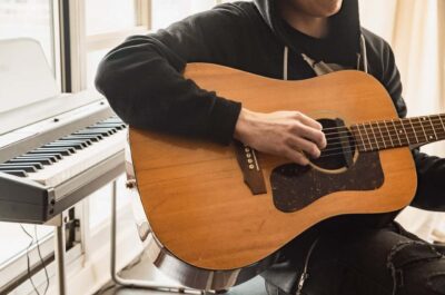 Man playing acoustic guitar with keyboard in background