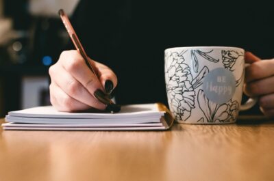 Person writing in notebook next to teacup