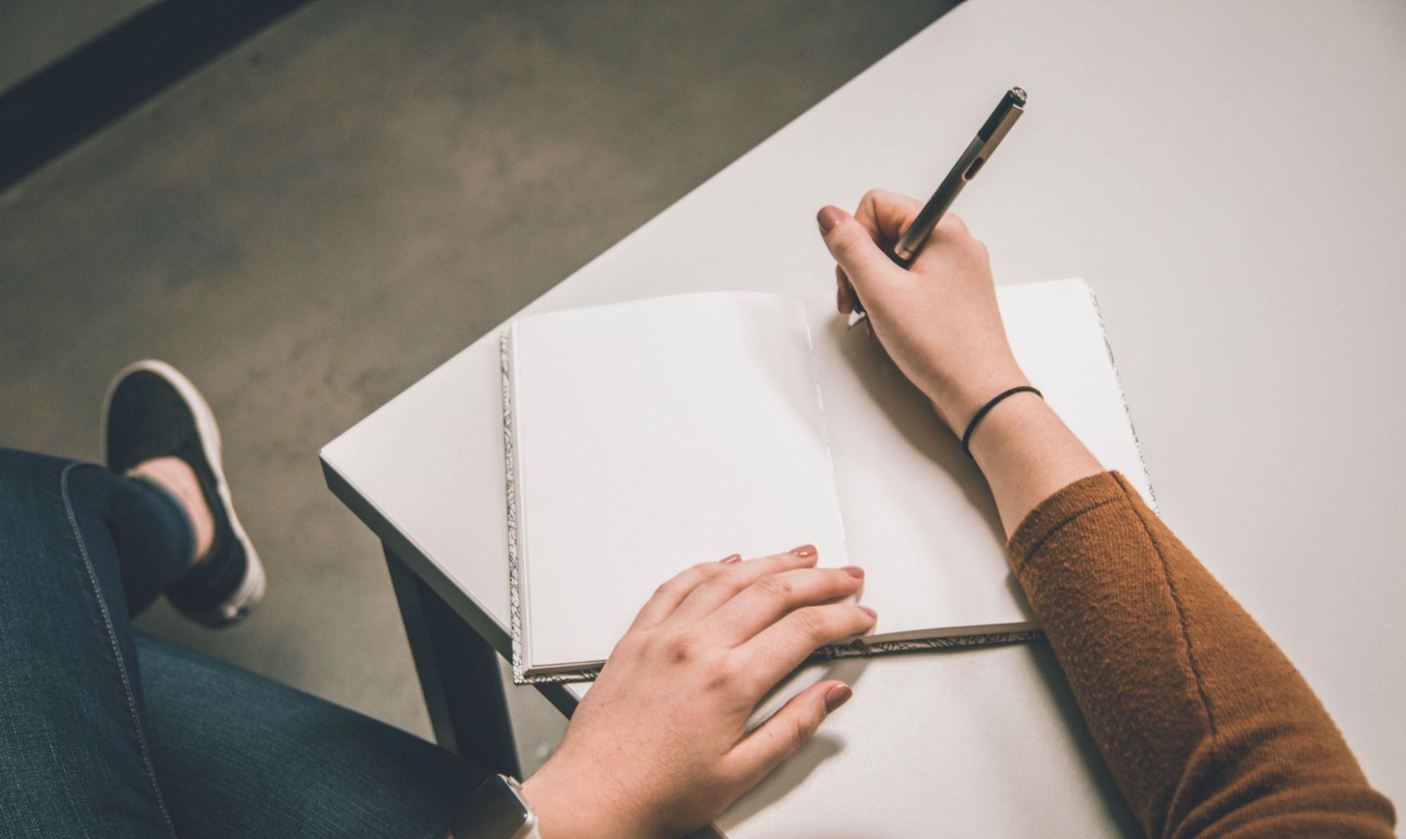 Person sitting at desk holding pen to paper