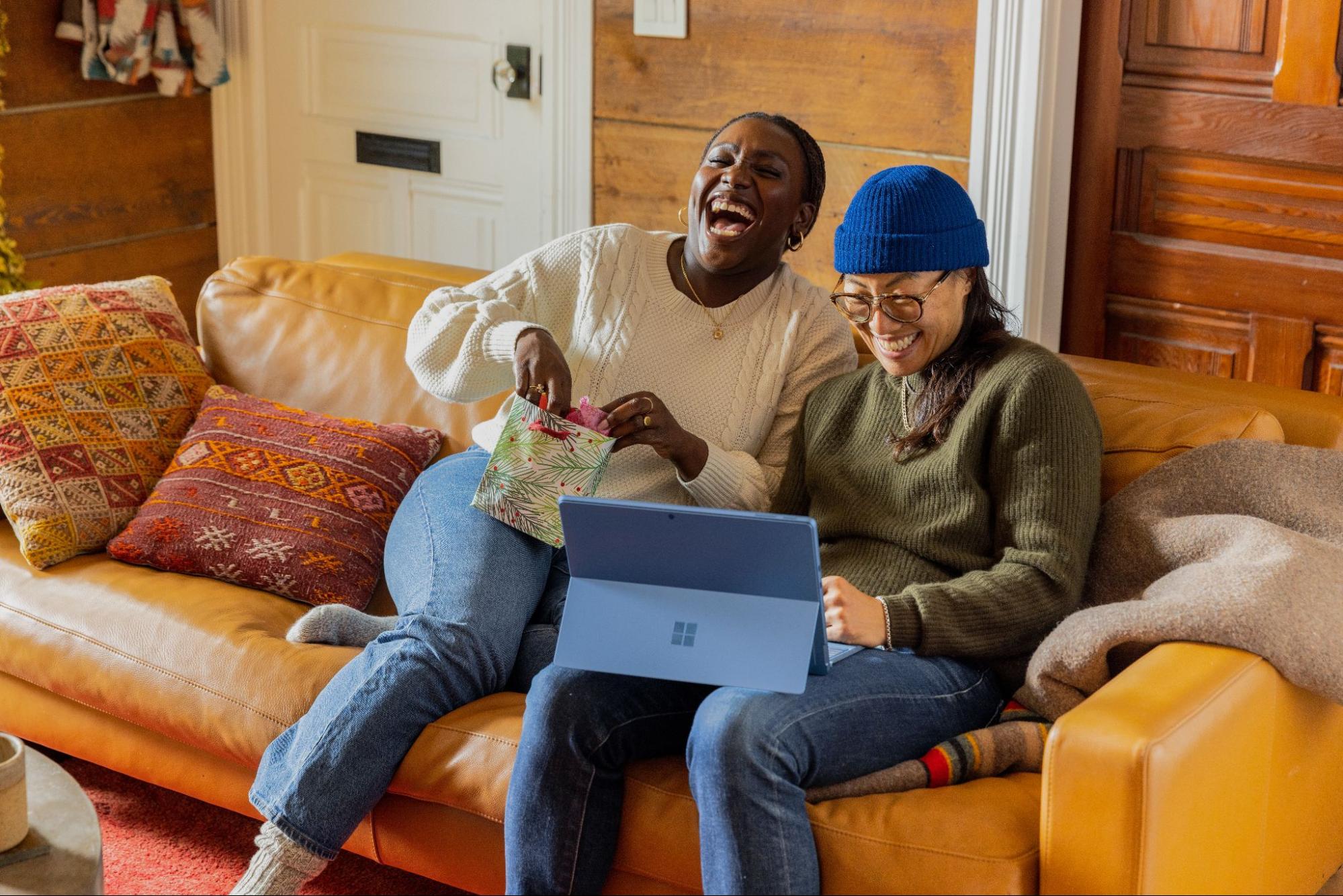 Two people sitting con couch laughing at laptop