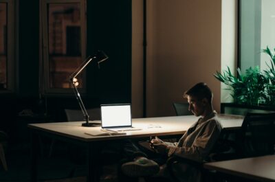 Person sitting on phone in dark room in front of laptop