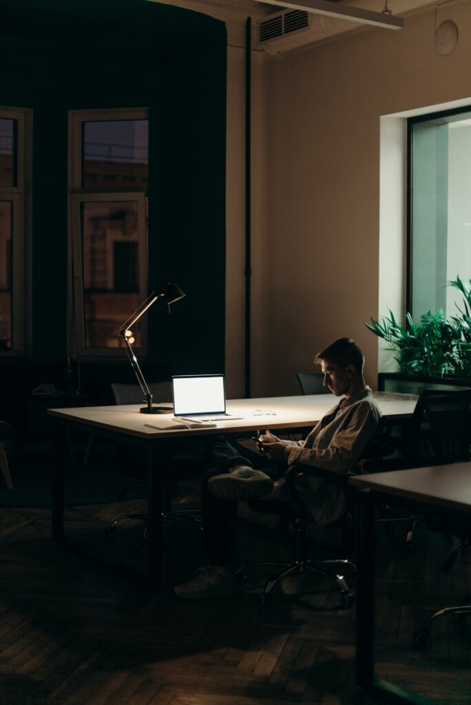 Person sitting on phone in dark room in front of laptop