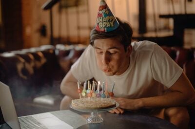 Person blowing out candles on cake in front of laptop