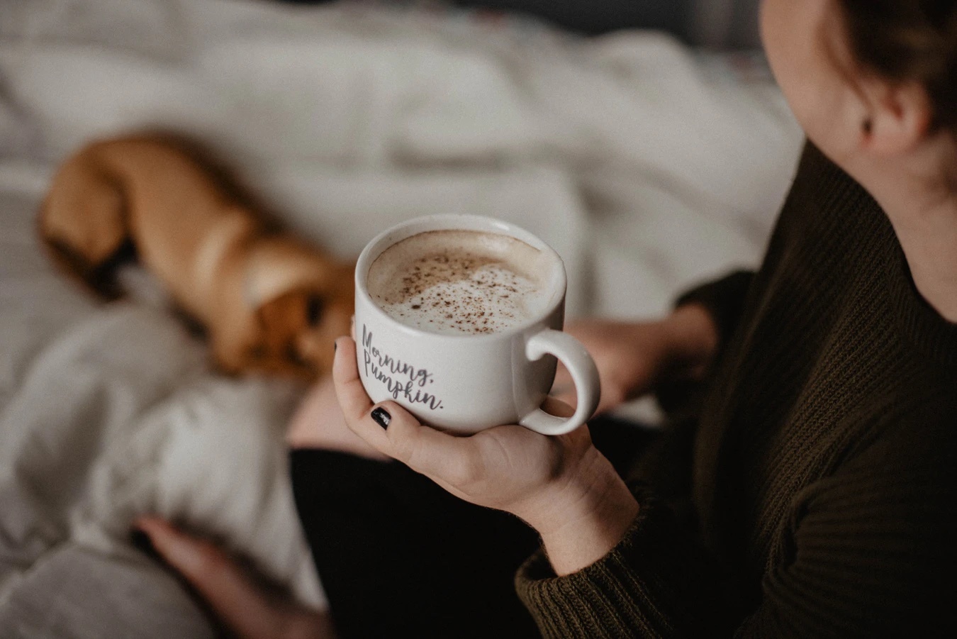Person holding cup of coffee in bed